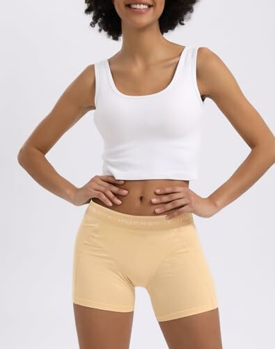 Mujer con ropa deportiva, top blanco y shorts beige.